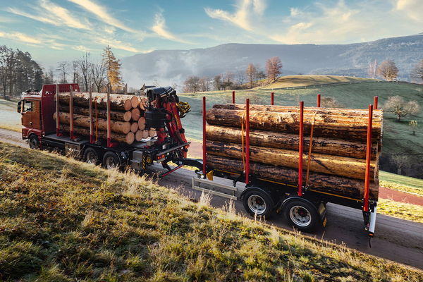 LKW mit Zentralachsanhänger von DOLL fährt im Morgengrauen über eine schmale Landstraße zwischen Wiesen und Feldern