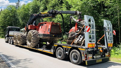 Schwerlasttraktor auf einem Tieflader für den Transport auf einer Waldstraße bei sonnigem Wetter gesichert.